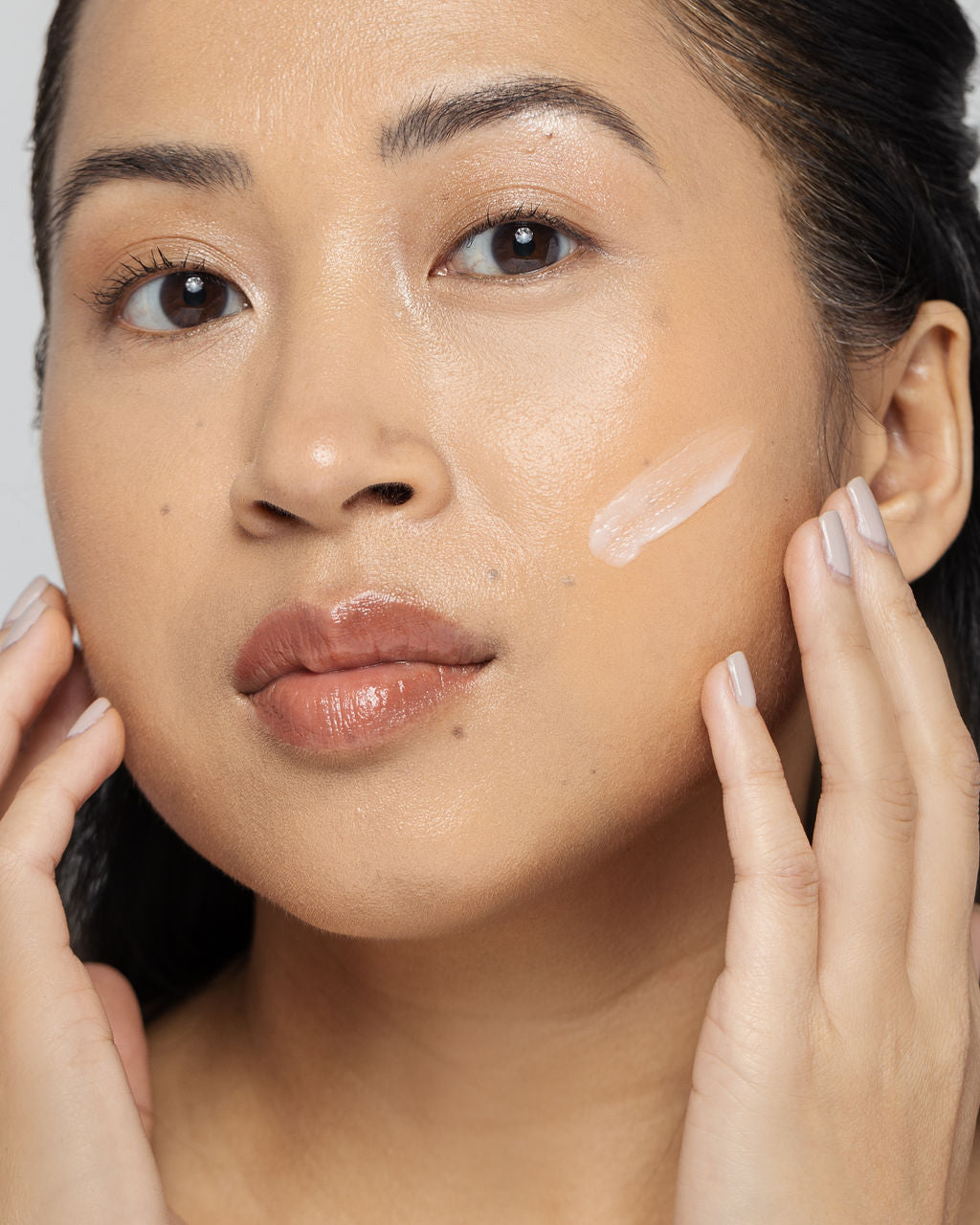 Close-up of a woman applying acne treatment lotion to her face, showcasing radiant, clear skin.