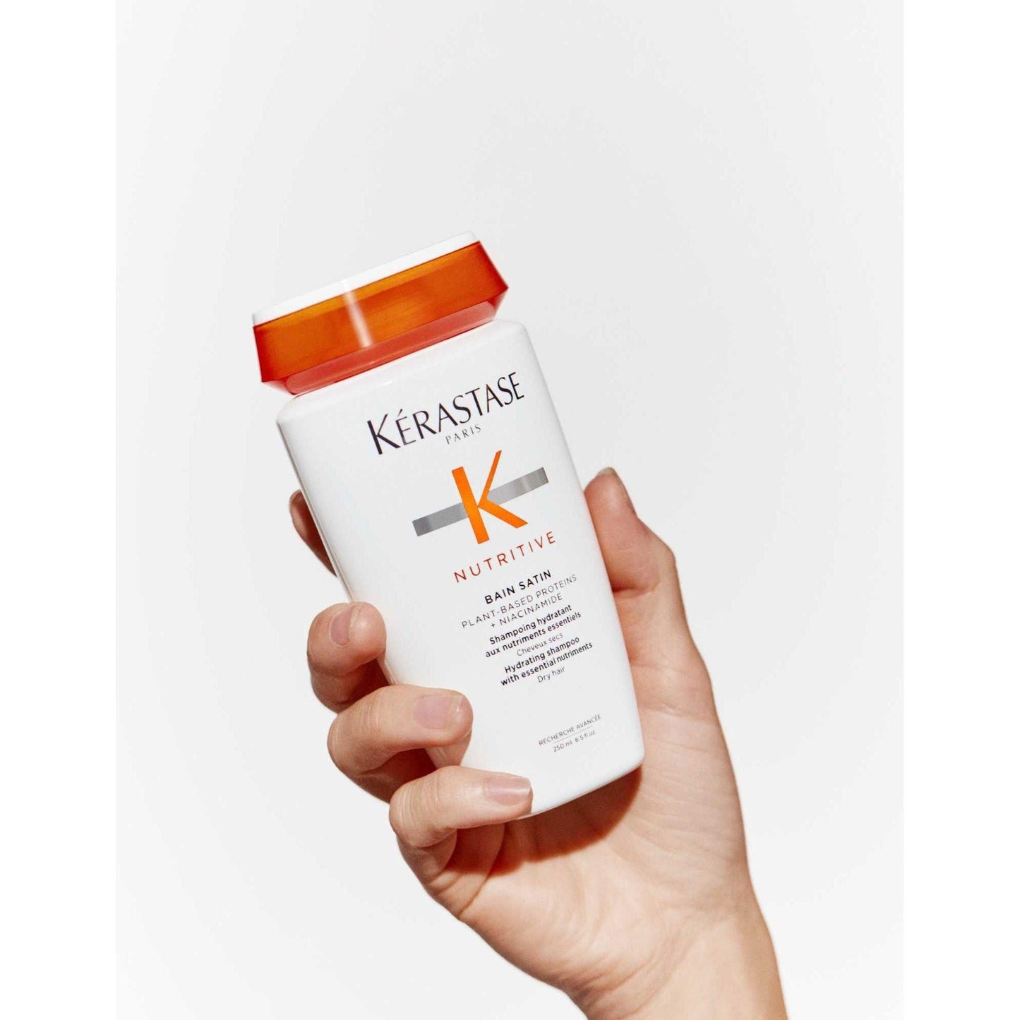 Hand holding Kérastase Nutritive Bain Satin shampoo for dry hair, showcasing its gentle moisturizing properties.