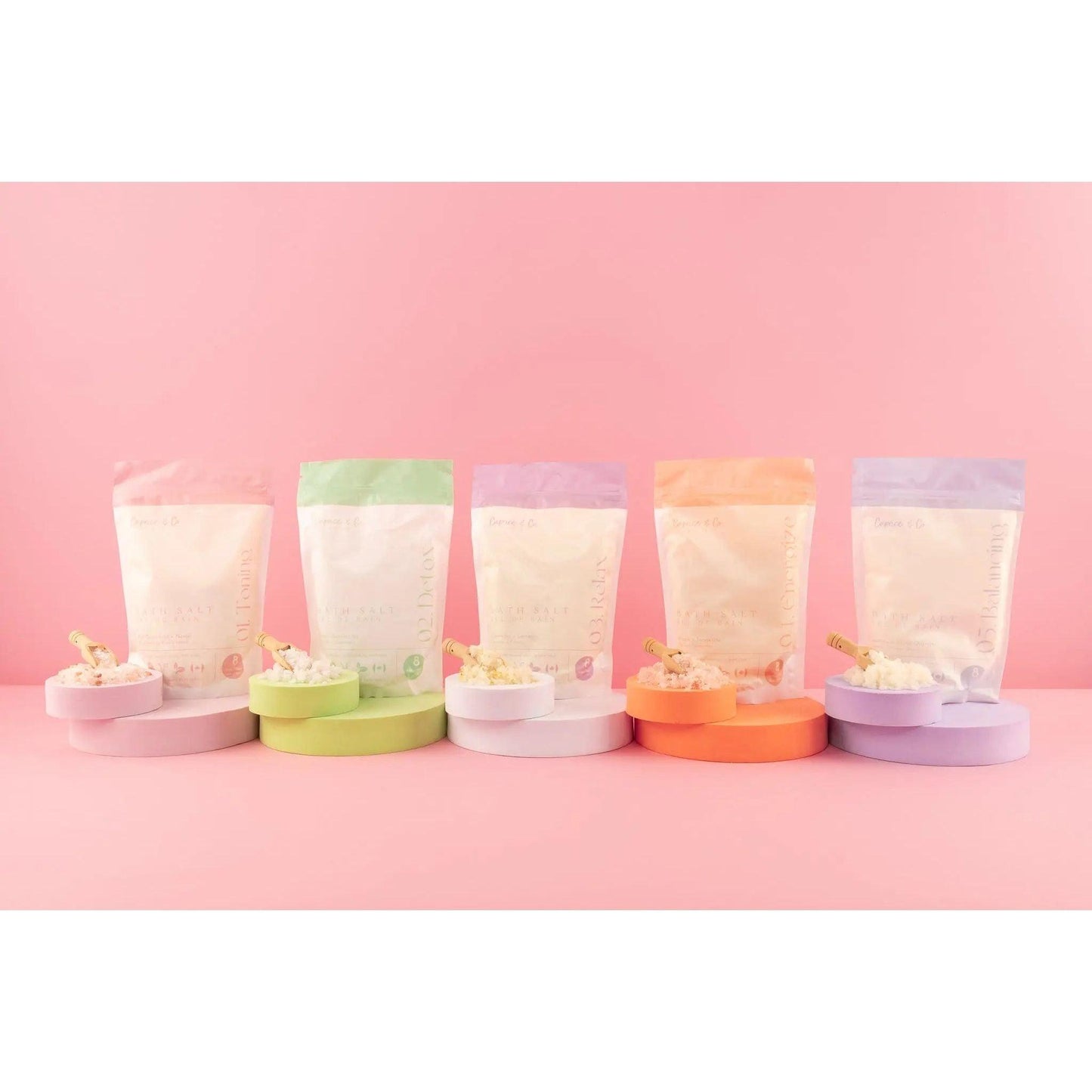 Colorful packaging of all-natural bath salts in different scents displayed on pastel background.
