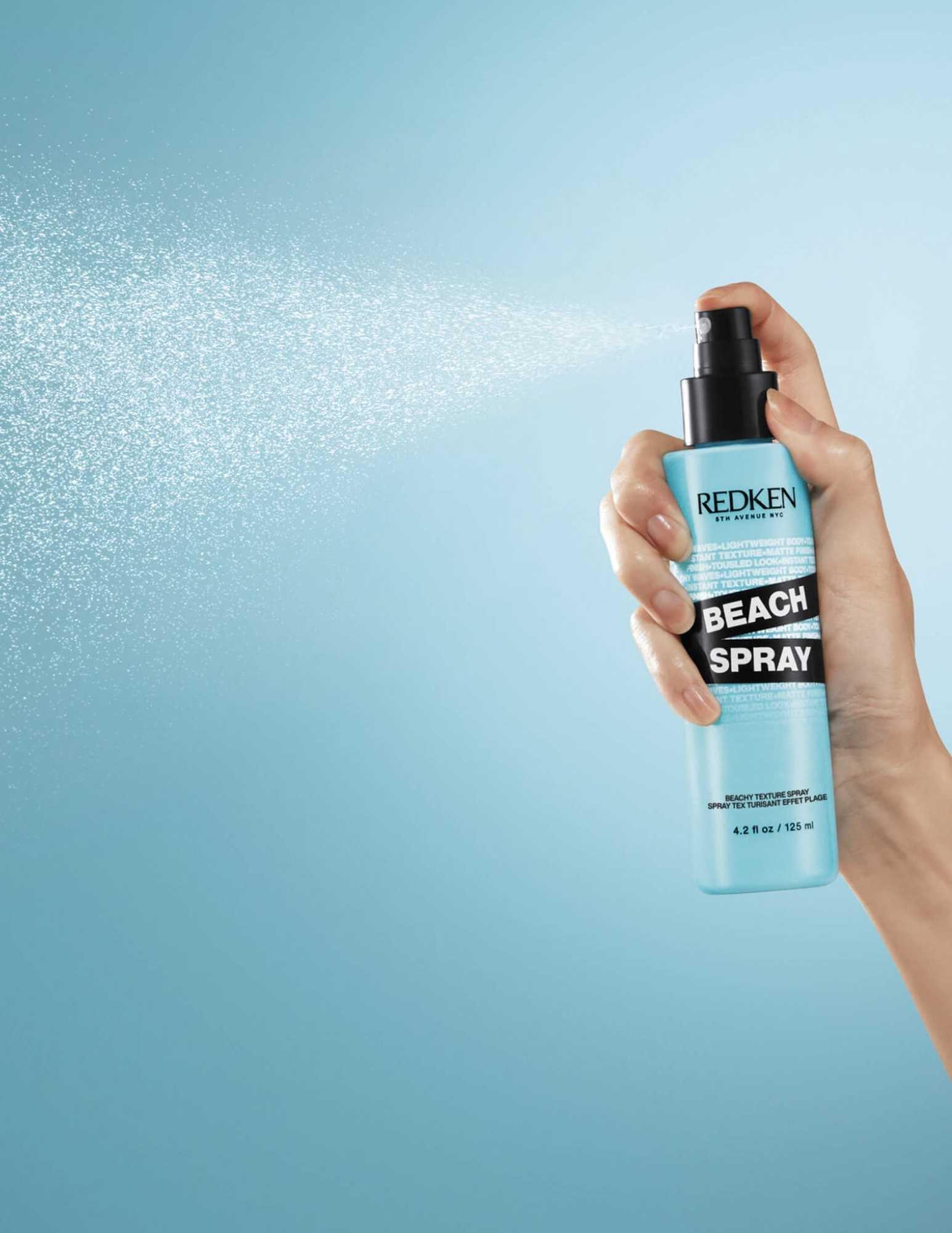 Redken Beach Spray bottle in hand, emitting a fine mist for texturized, beach-inspired hair. Perfect for all hair types.