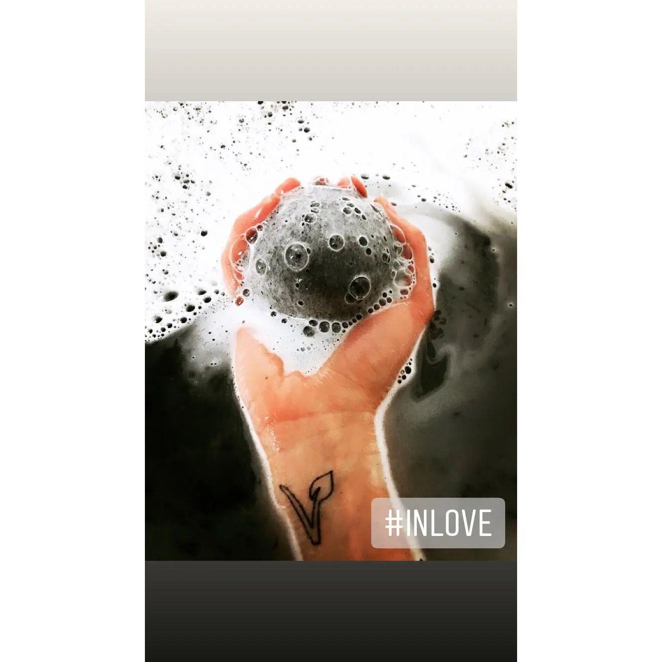 Hand holding a black bath bomb in bubbly water, showcasing relaxation and self-care.