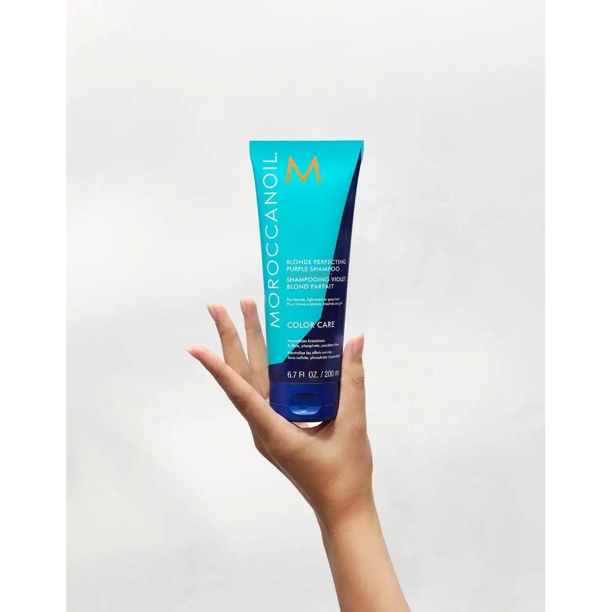 Moroccanoil Blonde Perfecting Purple Shampoo in a hand, showcasing its vibrant packaging for color-treated hair care.