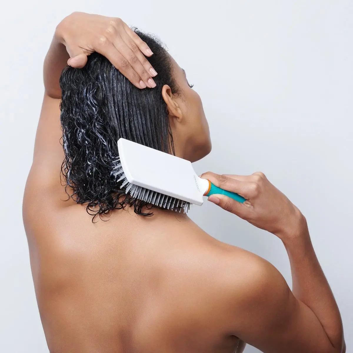 Woman using a Moroccanoil Ceramic Paddle Brush on wet hair, showcasing its high-quality ceramic and ionic properties.