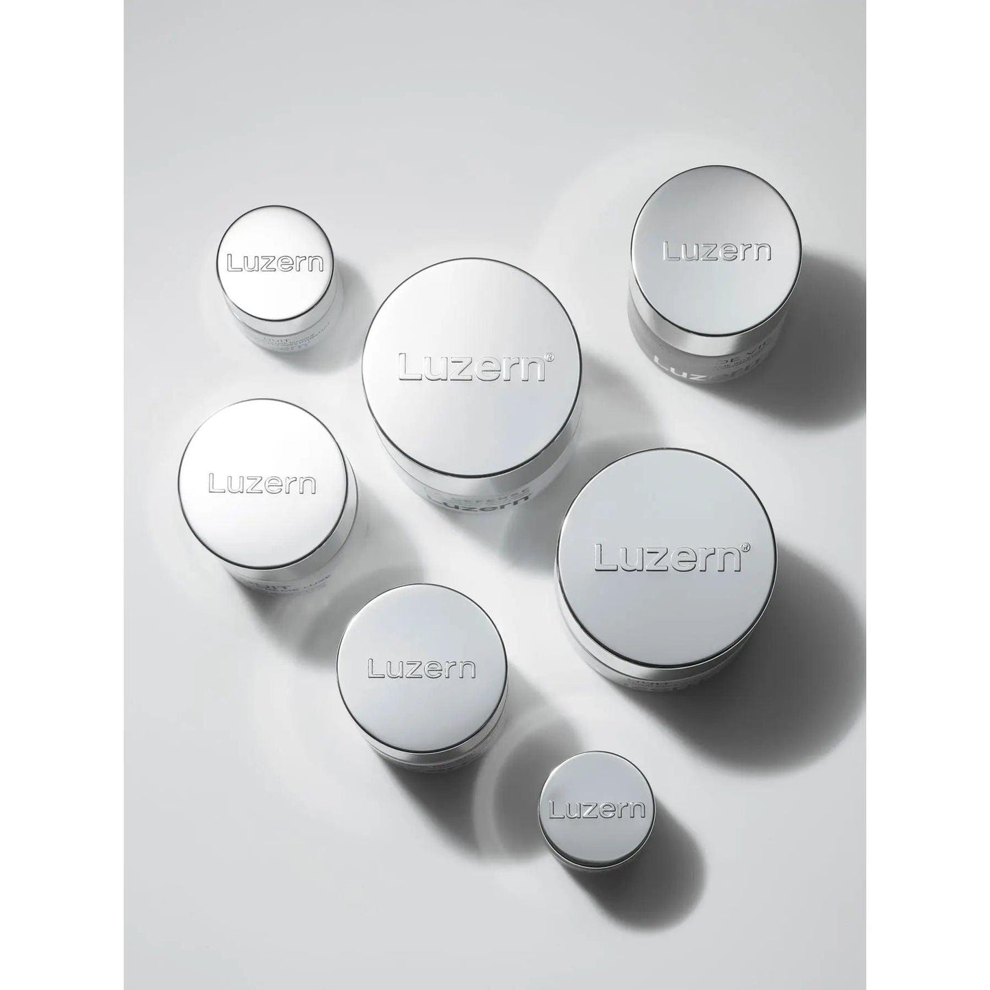 Various sizes of Luzern skincare cream jars with sleek silver packaging displayed on a light background.