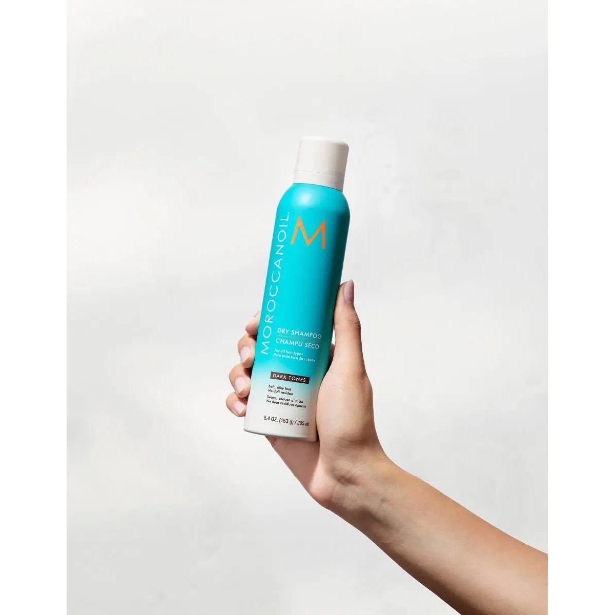 Moroccanoil Dry Shampoo for Dark Tones in hand, showcasing its blue bottle and UV-protecting, oil-absorbing formula.