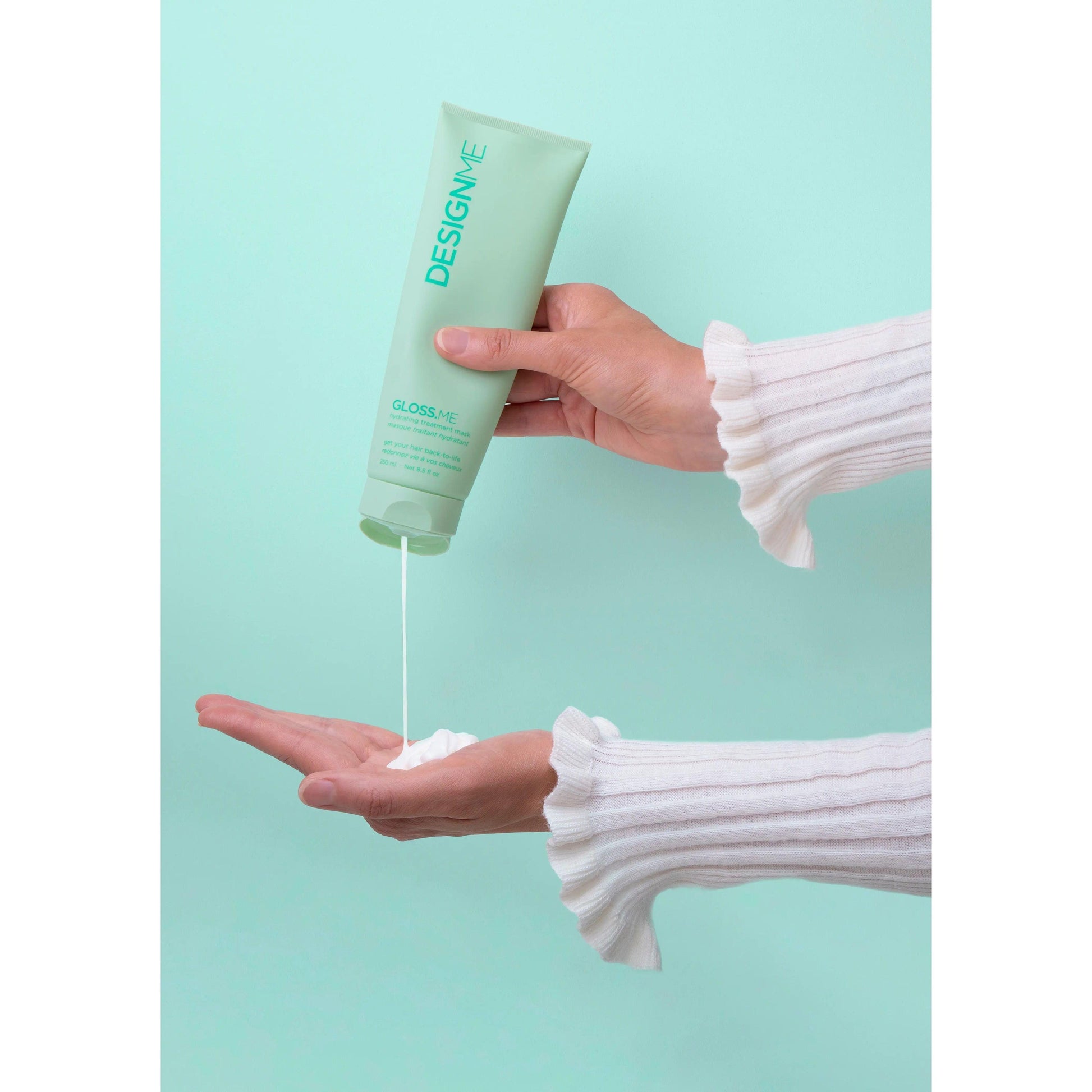 Person dispensing DESIGNME hair product into hand against a mint green background
