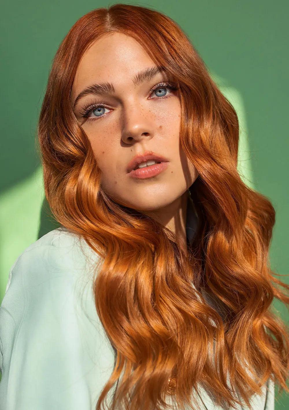 Model with shiny, wavy red hair showcasing healthy locks against a green background.