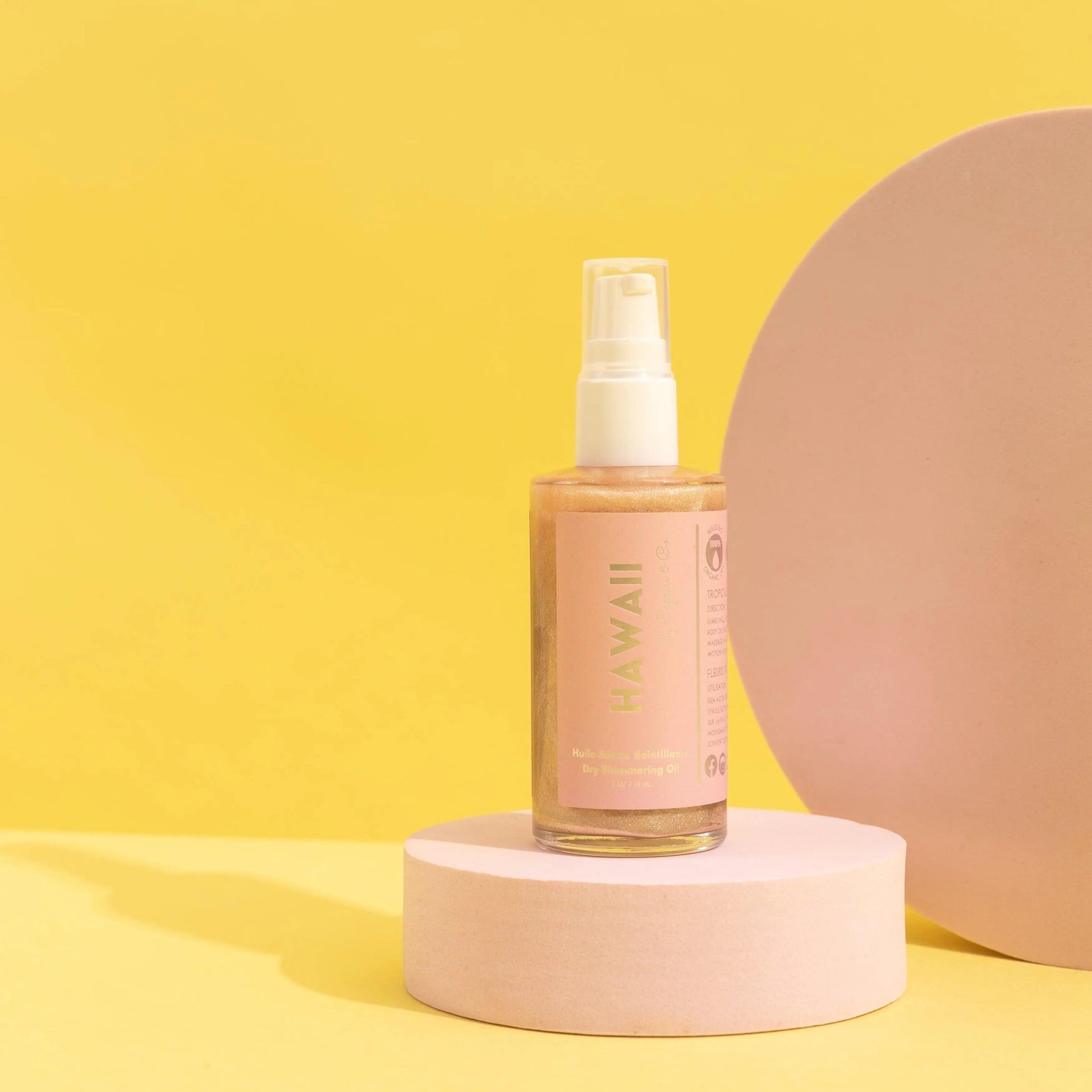 Hawaii Dry Shimmering Oil in a stylish bottle against a bright yellow background, showcasing its rose gold hue and elegant design.