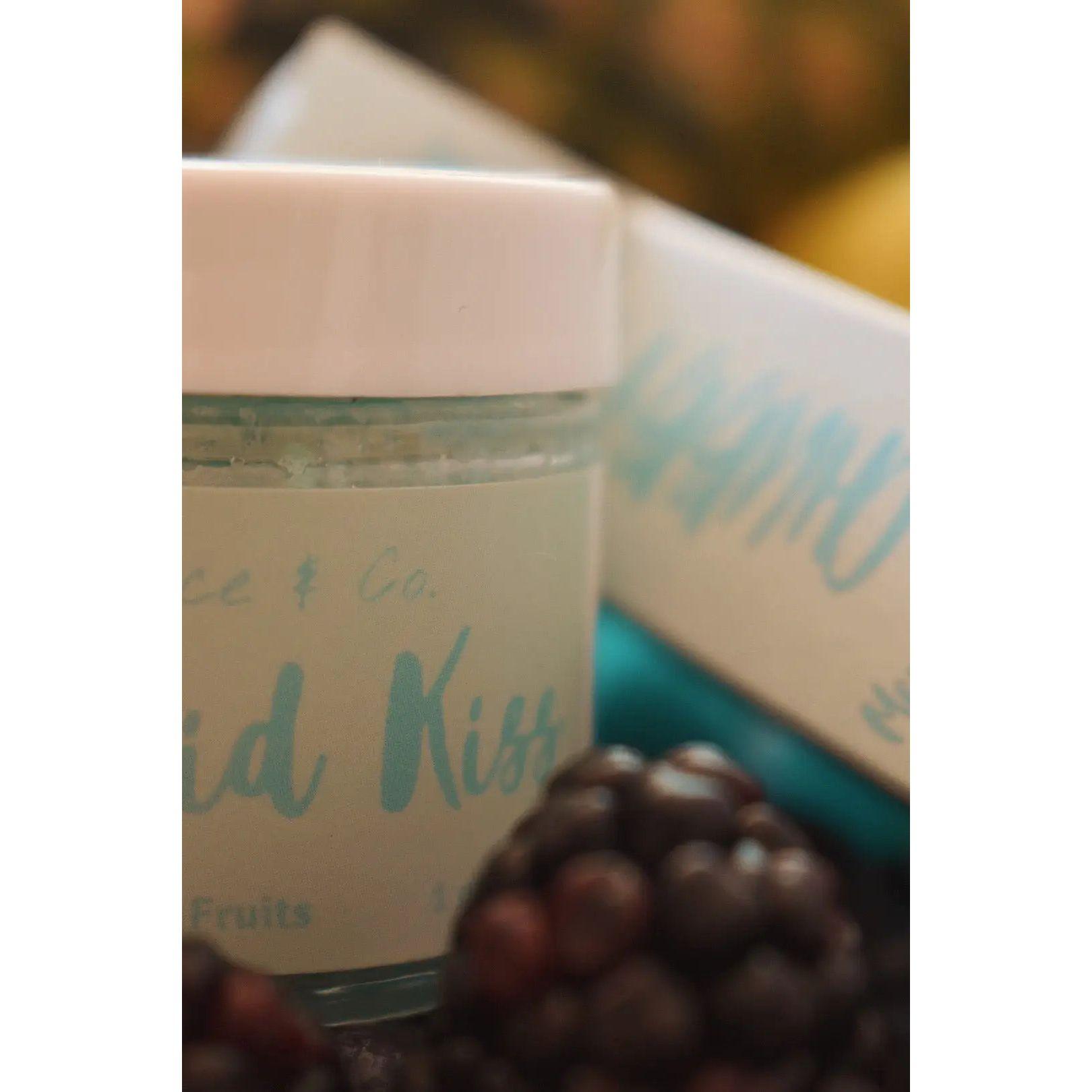 Close-up of Mermaid Kiss Lip Scrub jar surrounded by fresh blackberries, showcasing a sweet cotton candy scent.