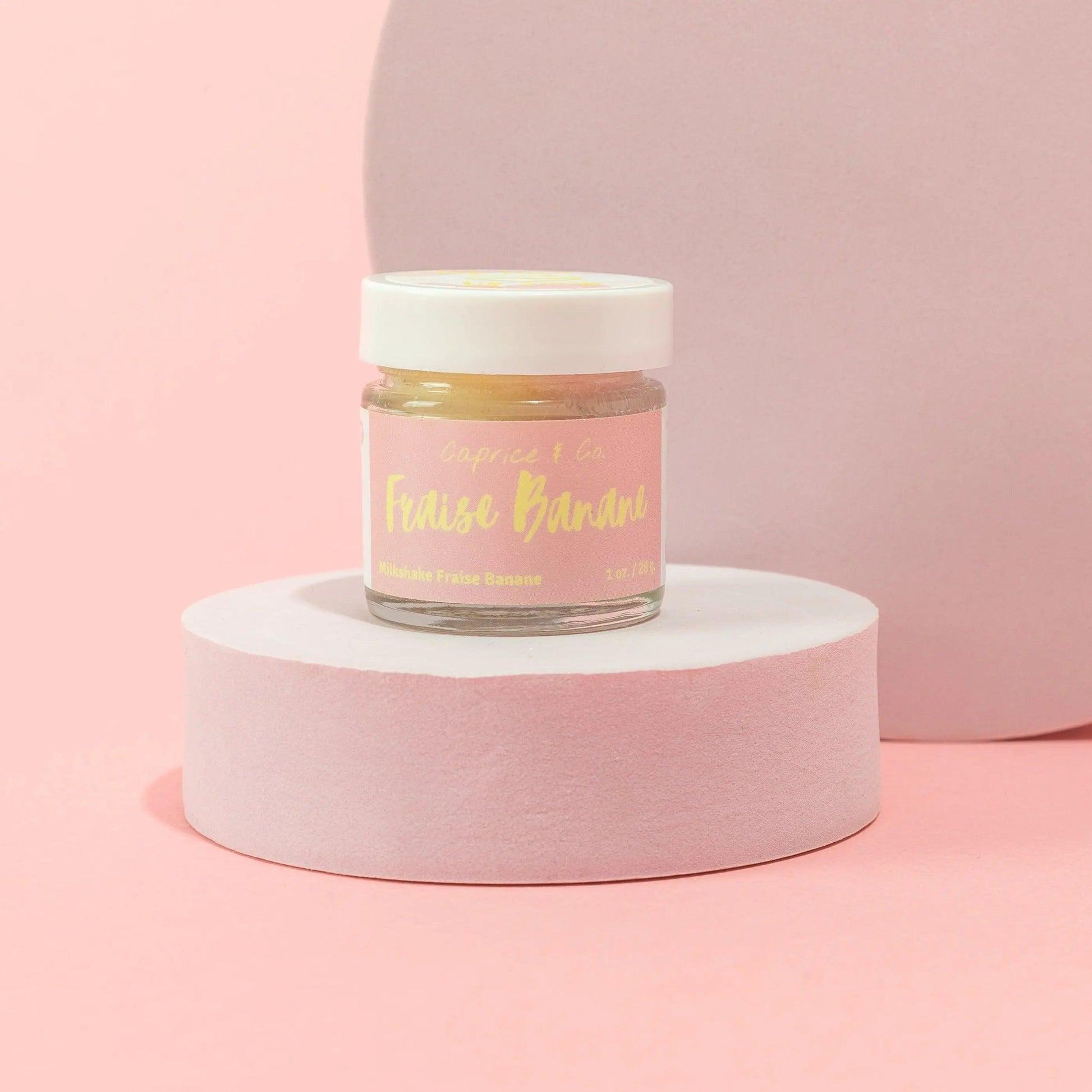 Strawberry banana lip scrub in a jar on a pink display, highlighting its sweet, edible formula for smooth lips.