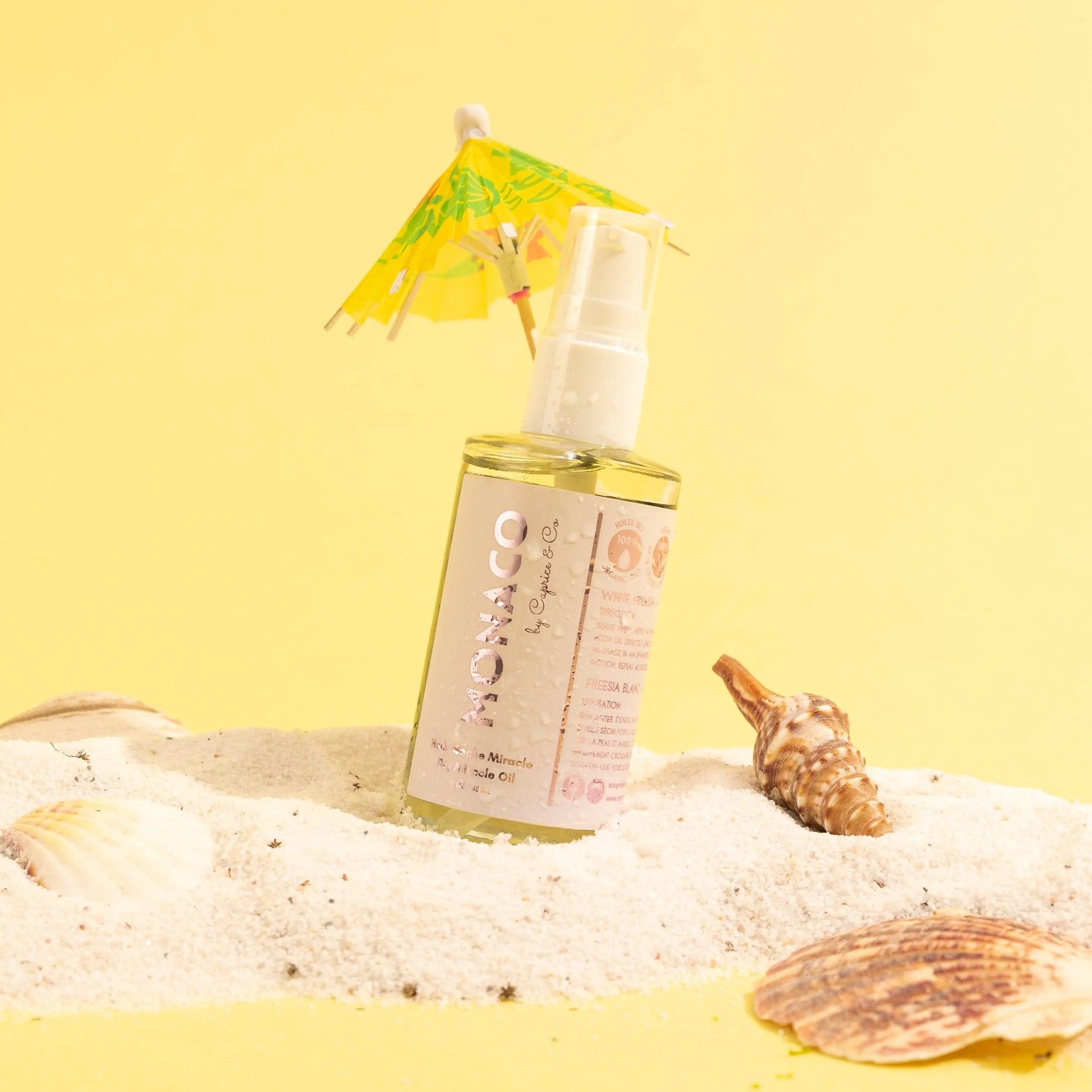 Monaco Dry Miracle Oil bottle with an umbrella, surrounded by seashells on a sunny beach backdrop.
