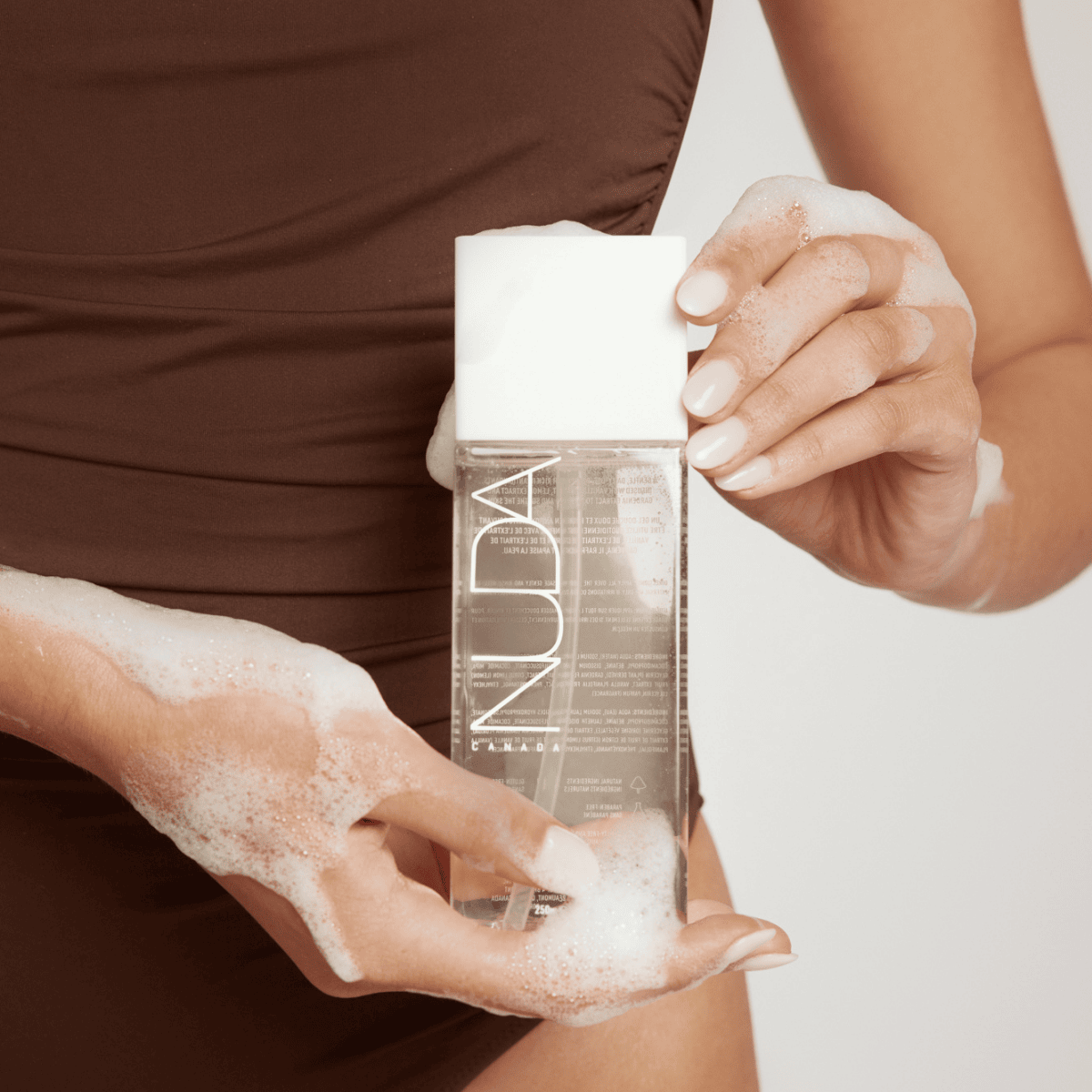Body Wash bottle held by a woman with suds, showcasing sunless tanning aftercare benefits.