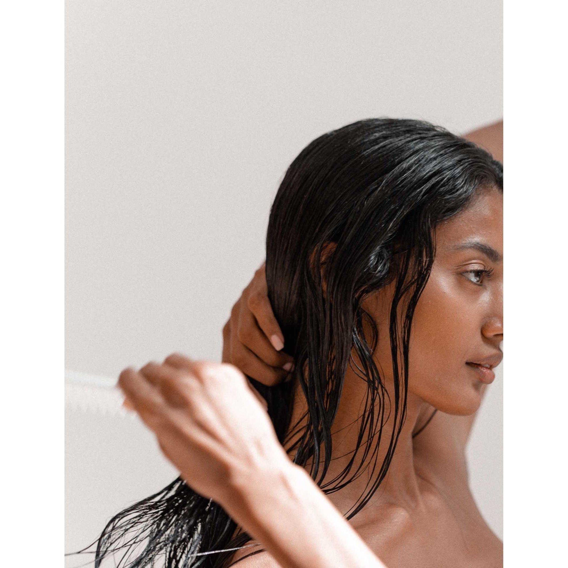 Woman with long, shiny hair combing her wet hair, showcasing healthy hair care routine and beauty rituals.