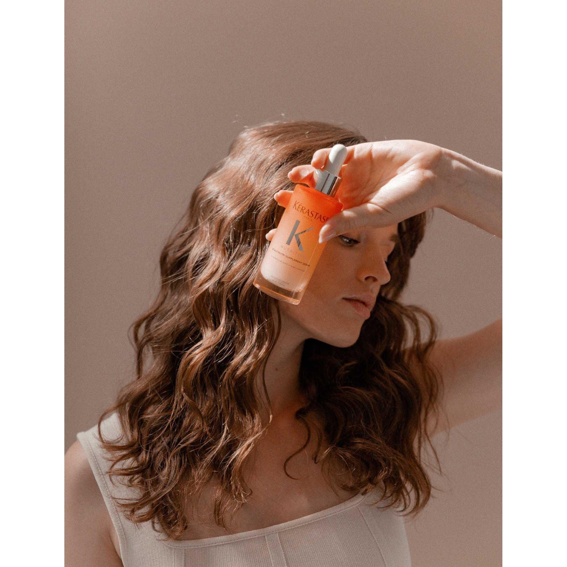 Model holding Kérastase Nutri-Supplement Scalp Serum, showcasing its nourishing properties for dry scalps.