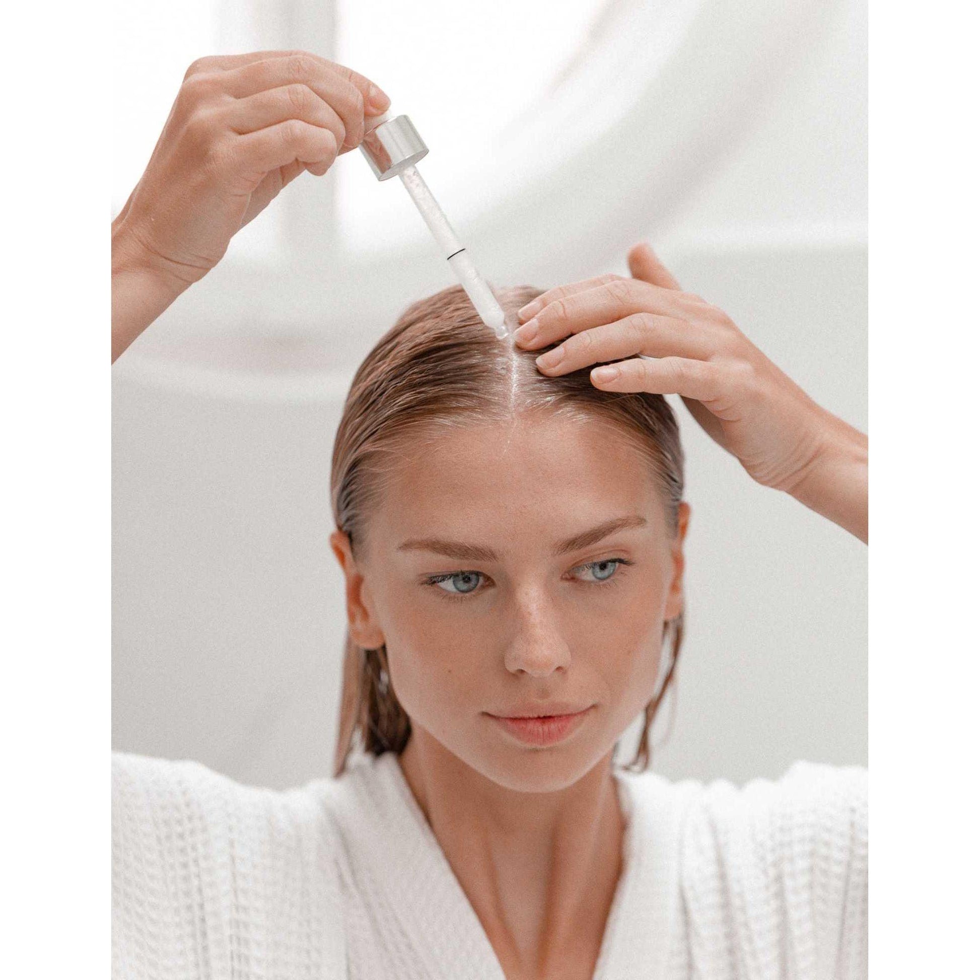 Woman applying Kérastase Nutri-Supplement Scalp Serum with a dropper for healthy scalp nourishment.