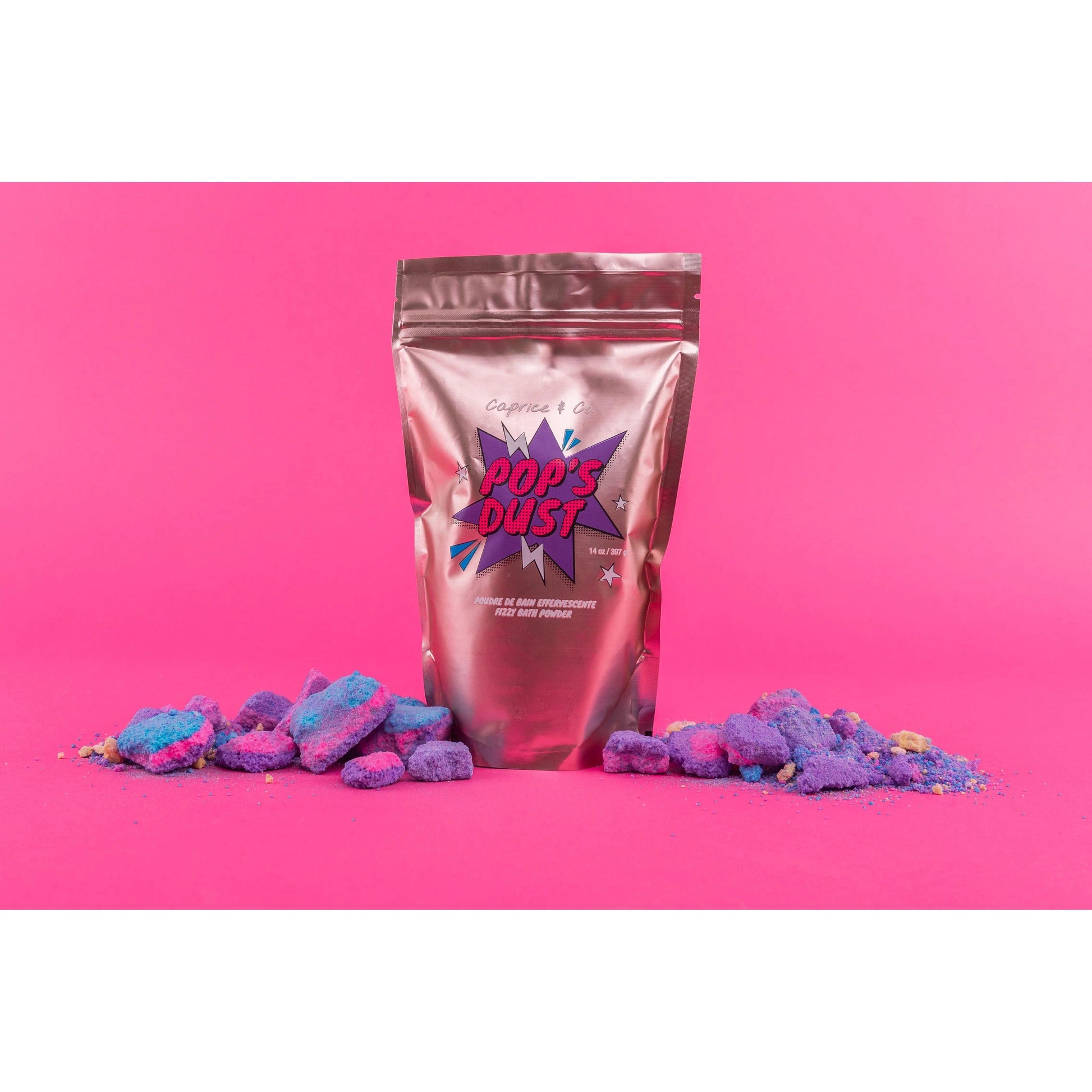 Pop's Dust fizzy bath powder in a metallic bag, surrounded by colorful bath crystals on a vibrant pink background.