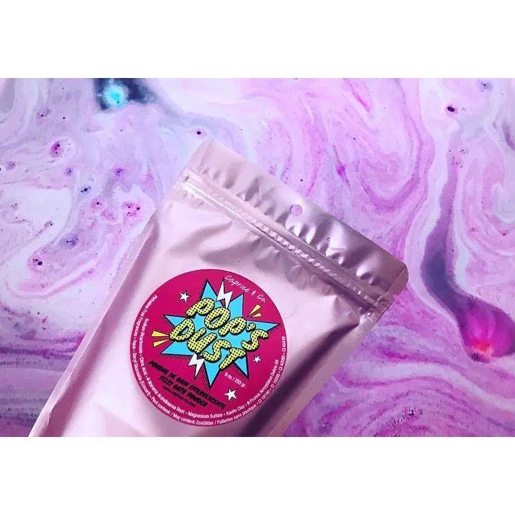 Pop's Dust fizzy bath powder packaging on a colorful marble background. 14 oz, sour candy scent for skin soothing.