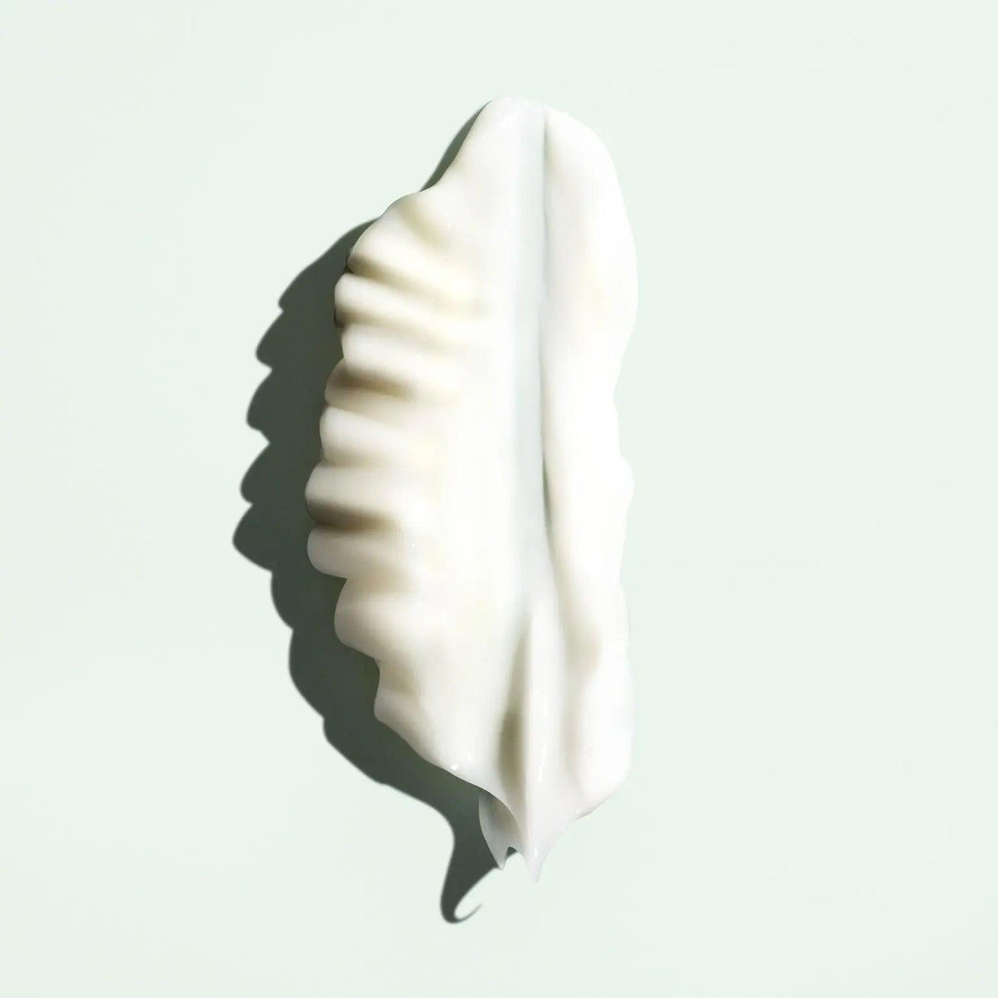 Silky white priming lotion leaf-shape detangler on a light green background, showcasing its smooth texture and hydrating properties.
