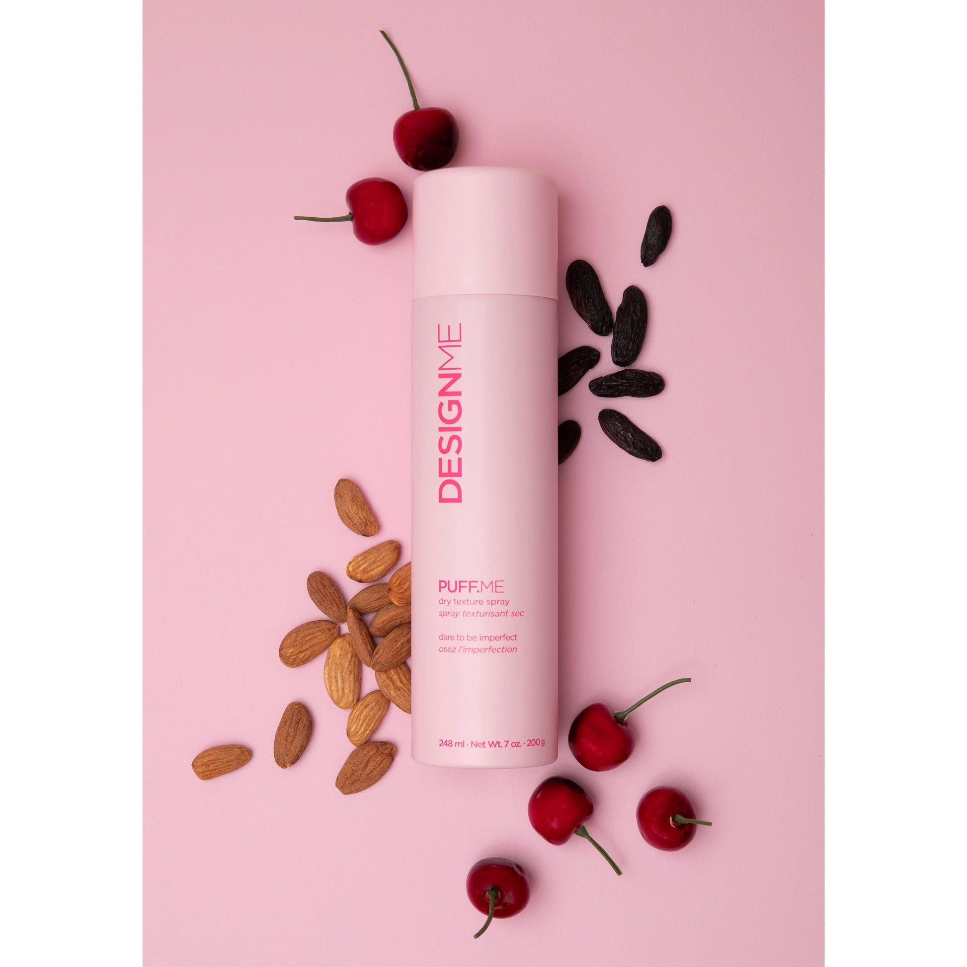 DesignME Puff Me hair product with almonds, cherries, and black seeds on a pink background