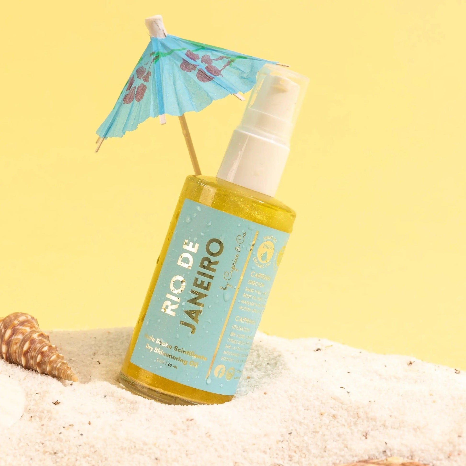Rio De Janeiro Dry Shimmering Oil bottle with beach umbrella on sand, showcasing a vibrant yellow gold color.