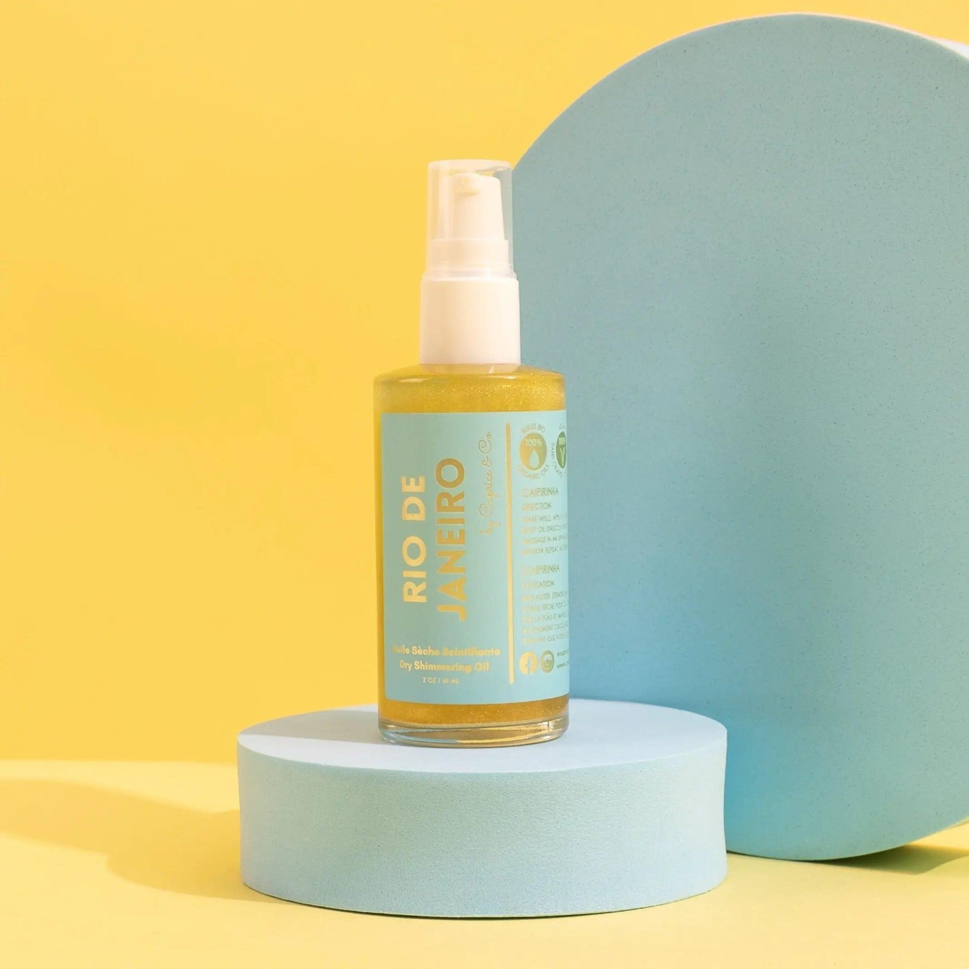 Rio De Janeiro Dry Shimmering Oil bottle on a blue pedestal, featuring lime and coconut water scent, yellow gold color.