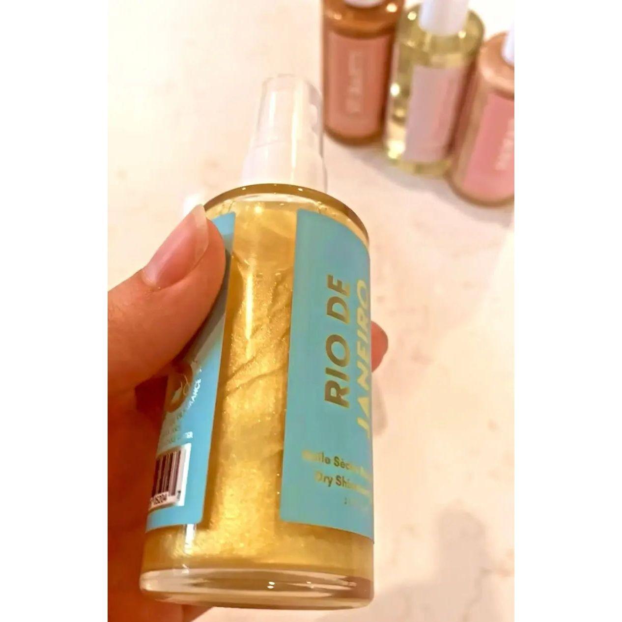 Hand holding Rio De Janeiro Dry Shimmering Oil bottle with yellow gold shimmer. Organic lime and coconut scent, 2 oz size.