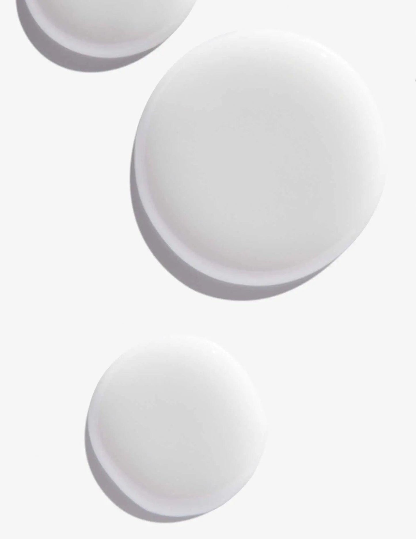 White round droplets of Scalp Relief Dandruff Shampoo on a light background, showcasing its smooth texture.