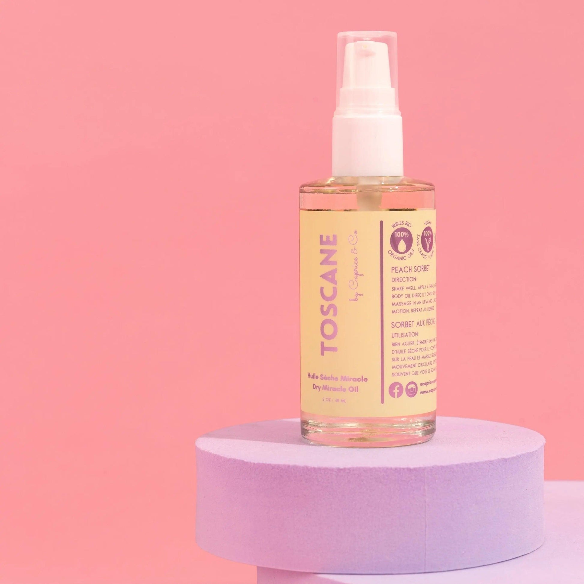 Toscane Dry Miracle Oil in Peach Sorbet scent, 2 oz bottle on pastel pedestal against pink background.