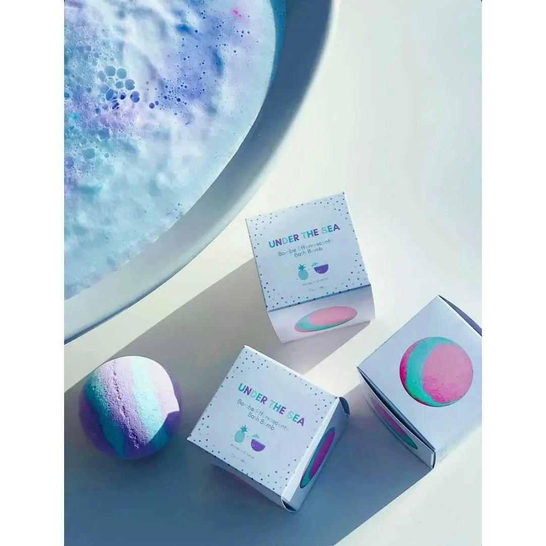 Under The Sea bath bombs with colorful packaging beside a bubbly bath for a tropical pineapple and coconut experience.