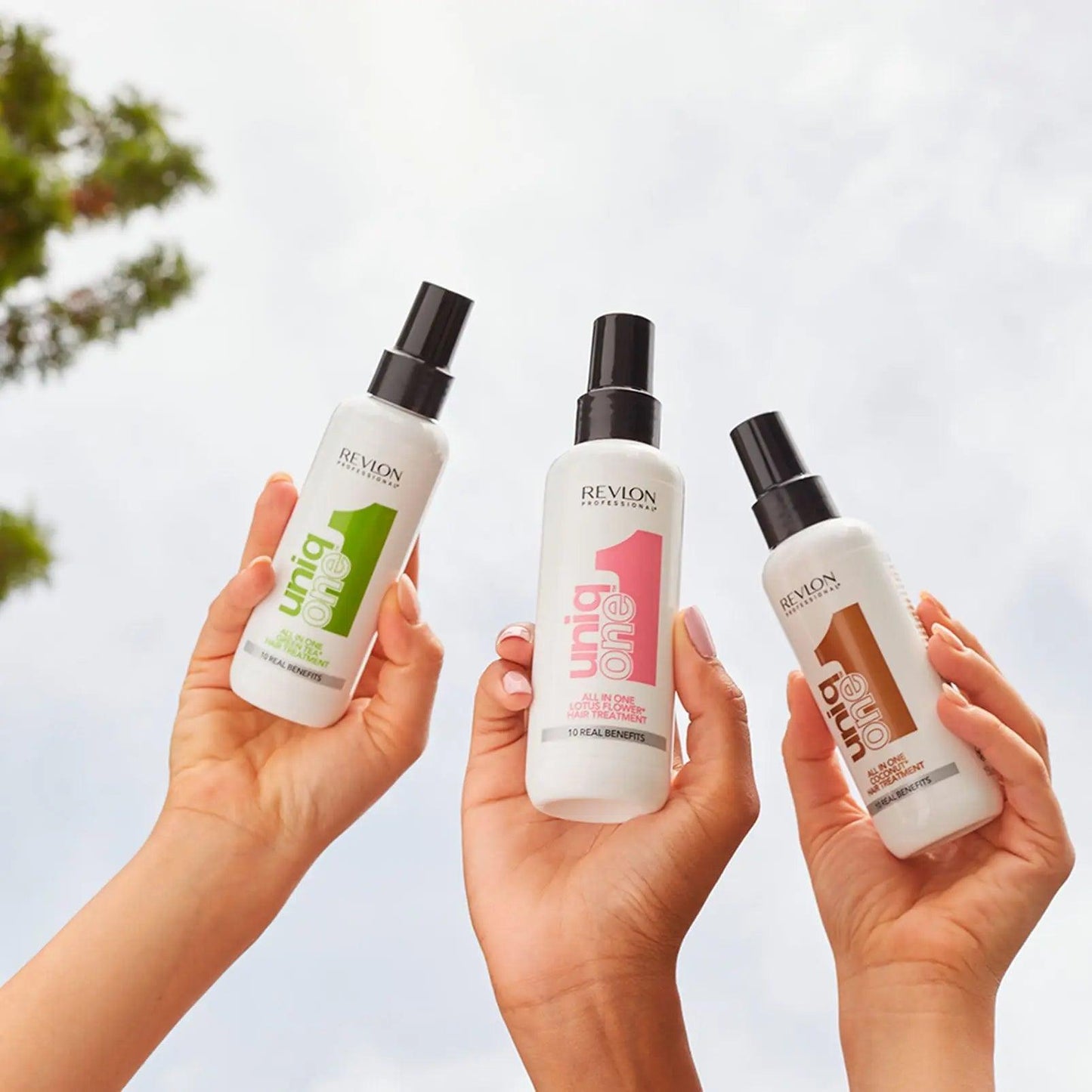 Three hands holding Revlon Uniq One Hair Treatment bottles against a sky background, featuring green, pink, and gold labels.