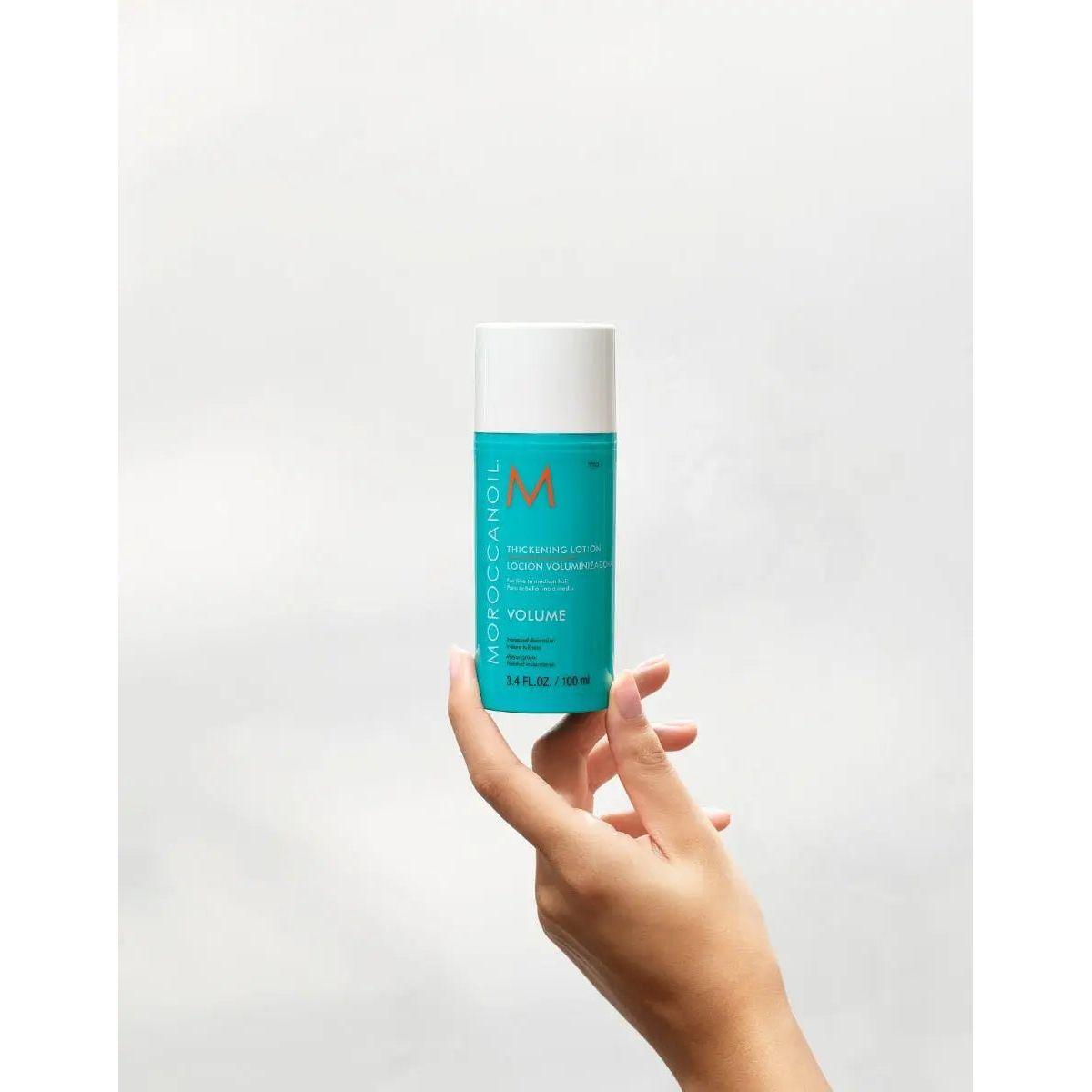 Moroccanoil® Volume Thickening Lotion held in hand, featuring its nourishing formula for fuller, shiny hair.