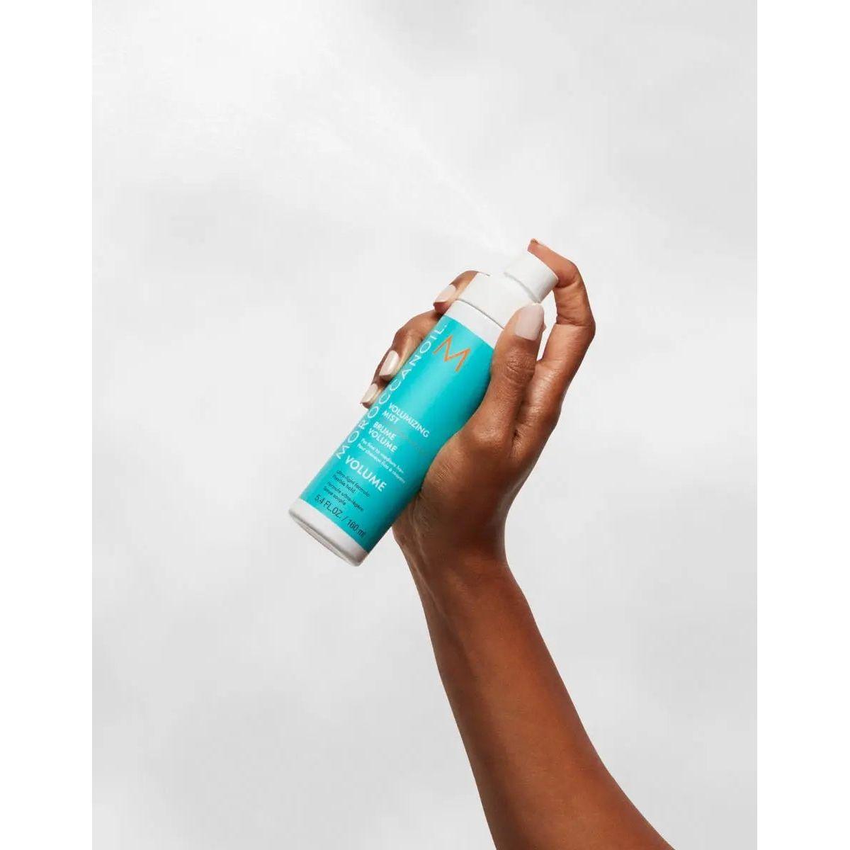 Hand holding a bottle of Volumizing Mist for fine, dull hair, promoting body and volume.