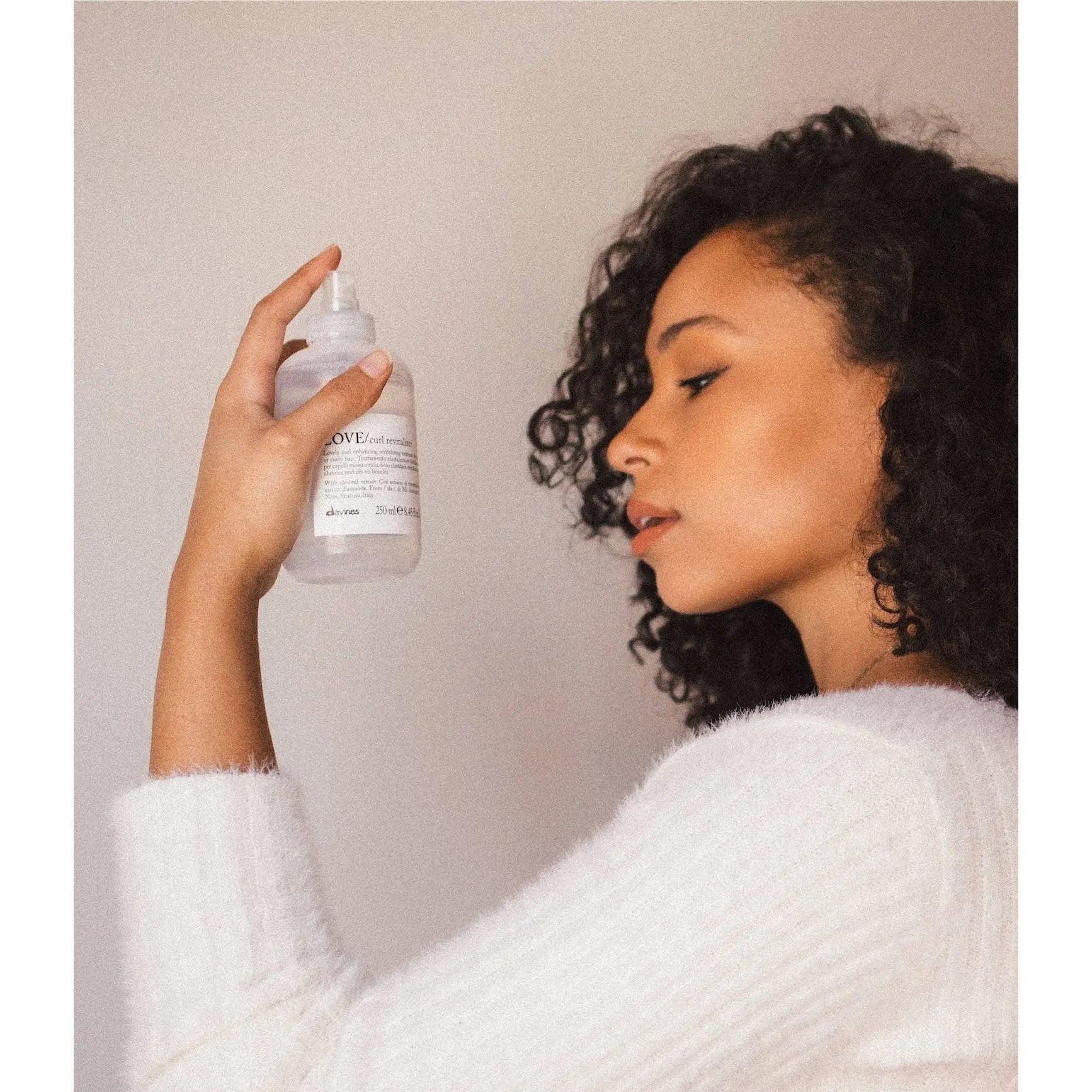 Woman with curly hair holding a bottle of LOVE Curl product, showcasing her curly hairstyle and beauty routine.