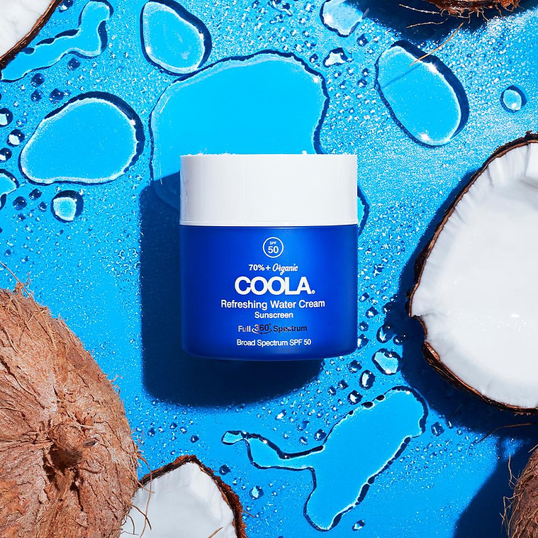 COOLA Full Spectrum 360º Refreshing Water Cream SPF 50 on a blue background with coconut halves and water droplets.