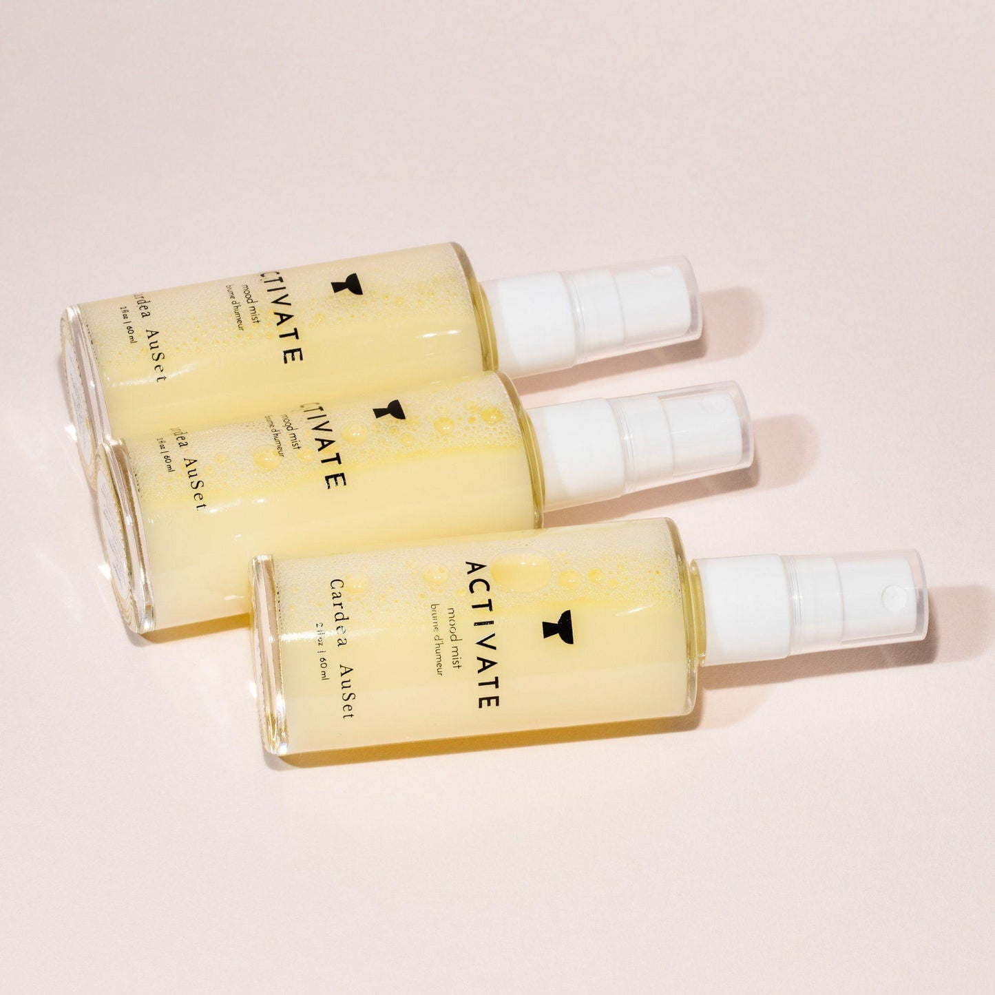 Three bottles of Activate facial spray laying on a beige background.