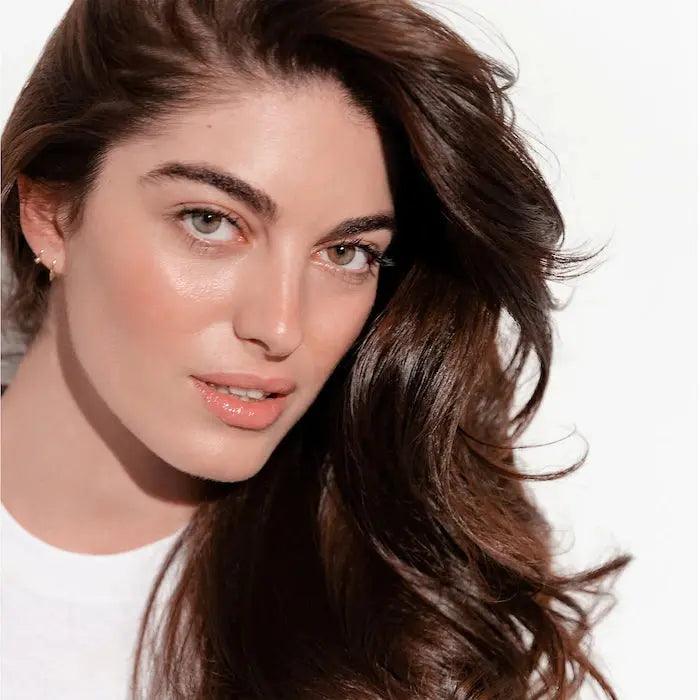 Woman with long brown hair and glowing skin looking at the camera