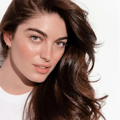 Woman with long brown hair and glowing skin looking at the camera