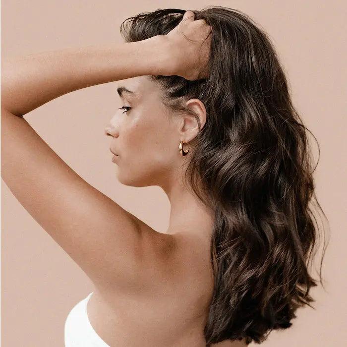 Woman with long, wavy hair posing in profile against a soft beige background