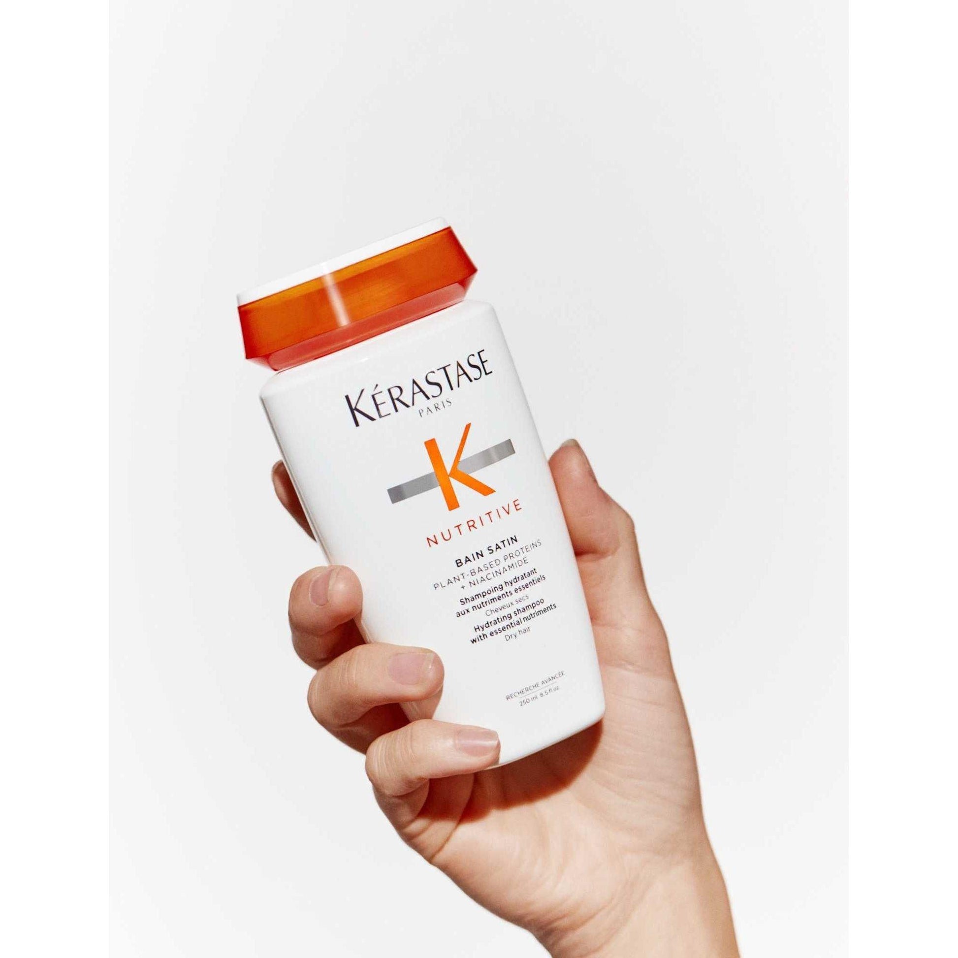 Hand holding Kérastase Nutritive Bain Satin shampoo for dry hair, showcasing its gentle moisturizing properties.