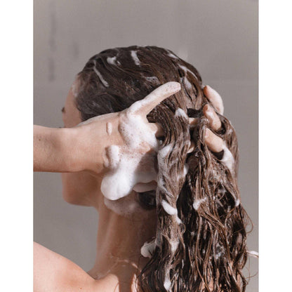 Woman applying moisturizing shampoo to her hair, showcasing nourishing foam and healthy hair texture.