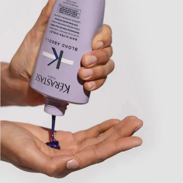 Person dispensing purple Kérastase Blond Absolu hair product into hand for blonde hair care.