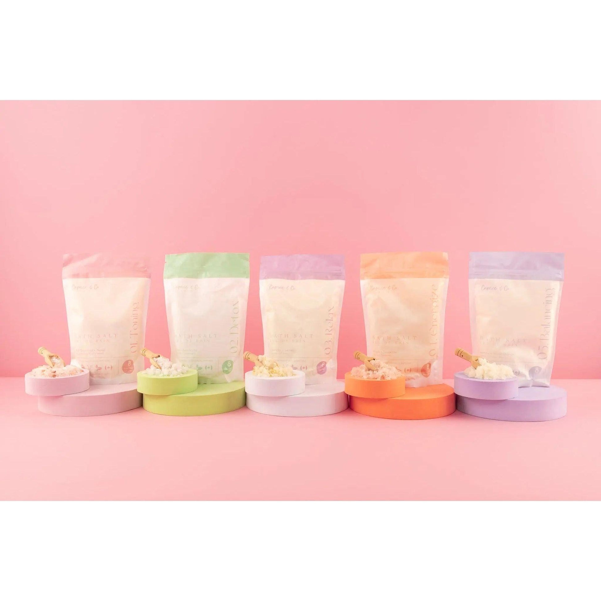 Colorful packaging of all-natural bath salts in different scents displayed on pastel background.
