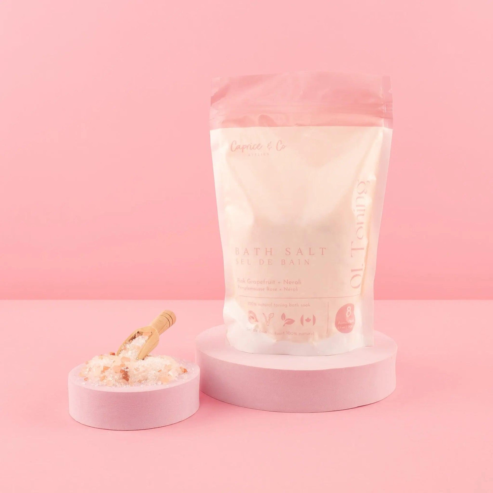All natural bath salts in a pink package with a scoop, set against a pastel pink background.