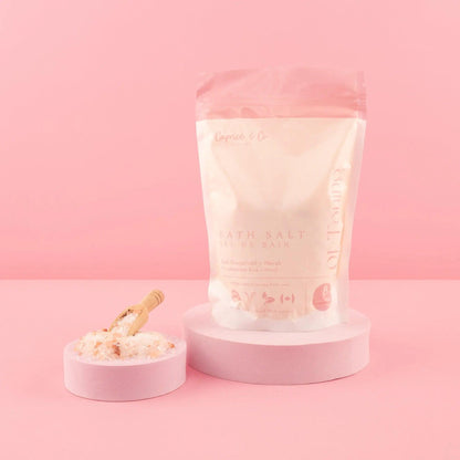 All natural bath salts in a pink package with a scoop, set against a pastel pink background.