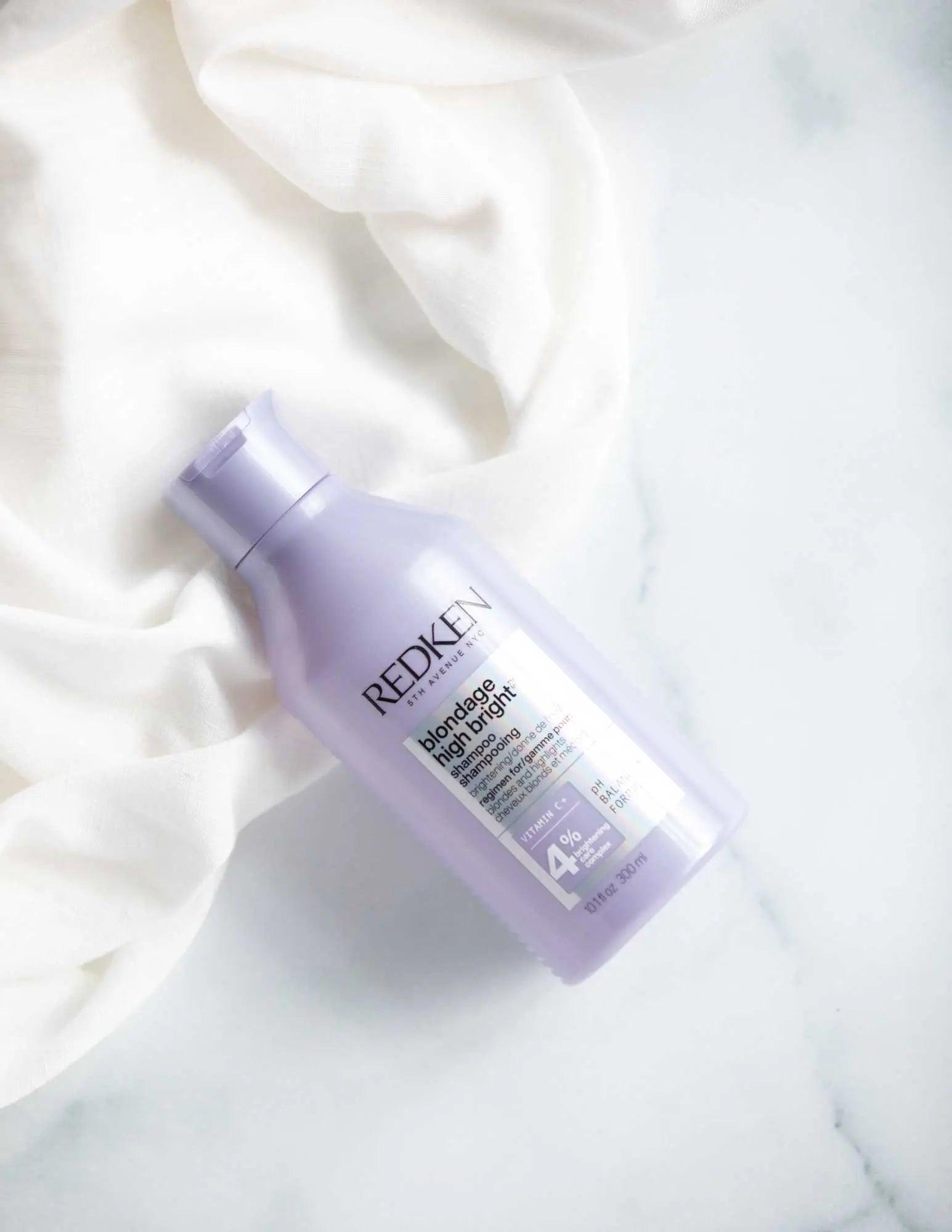 Redken Blondage High Bright Shampoo bottle on a soft fabric background, designed to enhance blonde hair vibrancy.