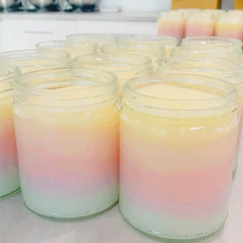 Colorful layered scented candles in glass jars with pastel hues of pink, yellow, and green, arranged on a kitchen countertop.