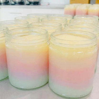 Colorful layered scented candles in glass jars with pastel hues of pink, yellow, and green, arranged on a kitchen countertop.