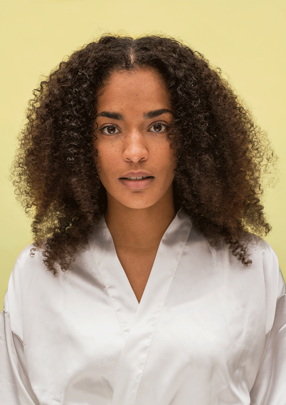 Woman with defined curly hair showcasing natural curls against a yellow background, highlighting the BOUNCE.ME Curl Glitz Kit results.