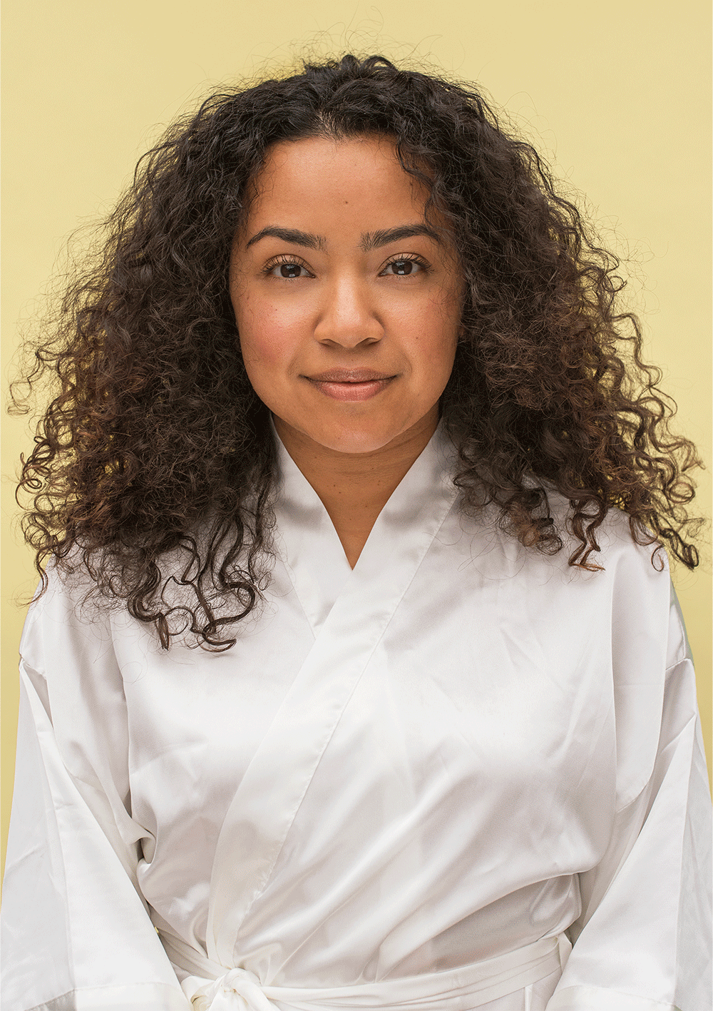 Woman with natural curly hair wearing a white robe, showcasing healthy curls and confident style.