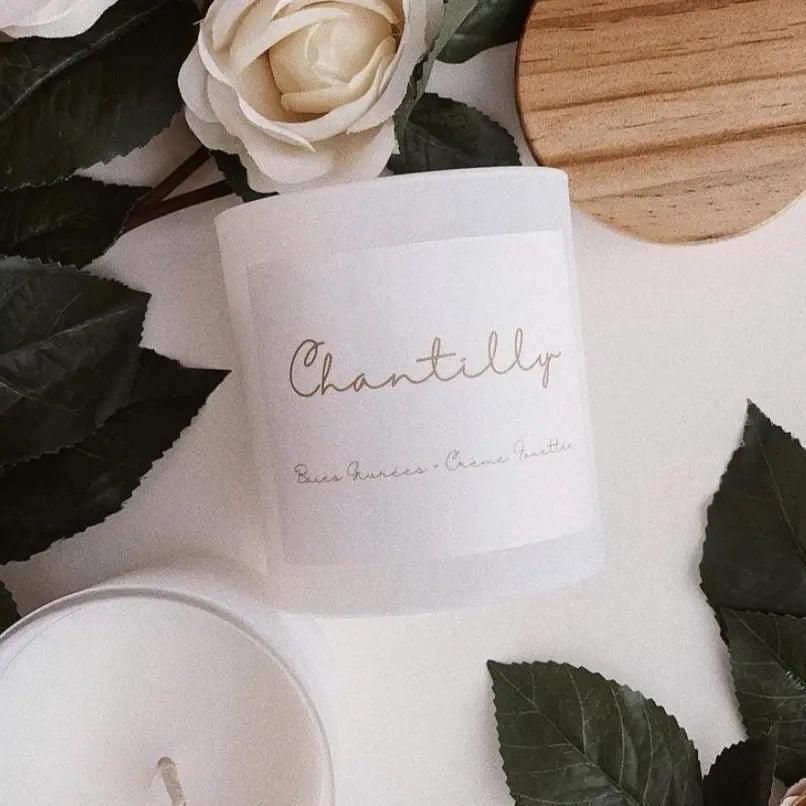 Chantilly candle with frosted berries scent, surrounded by leaves and a floral decor on a wooden surface.
